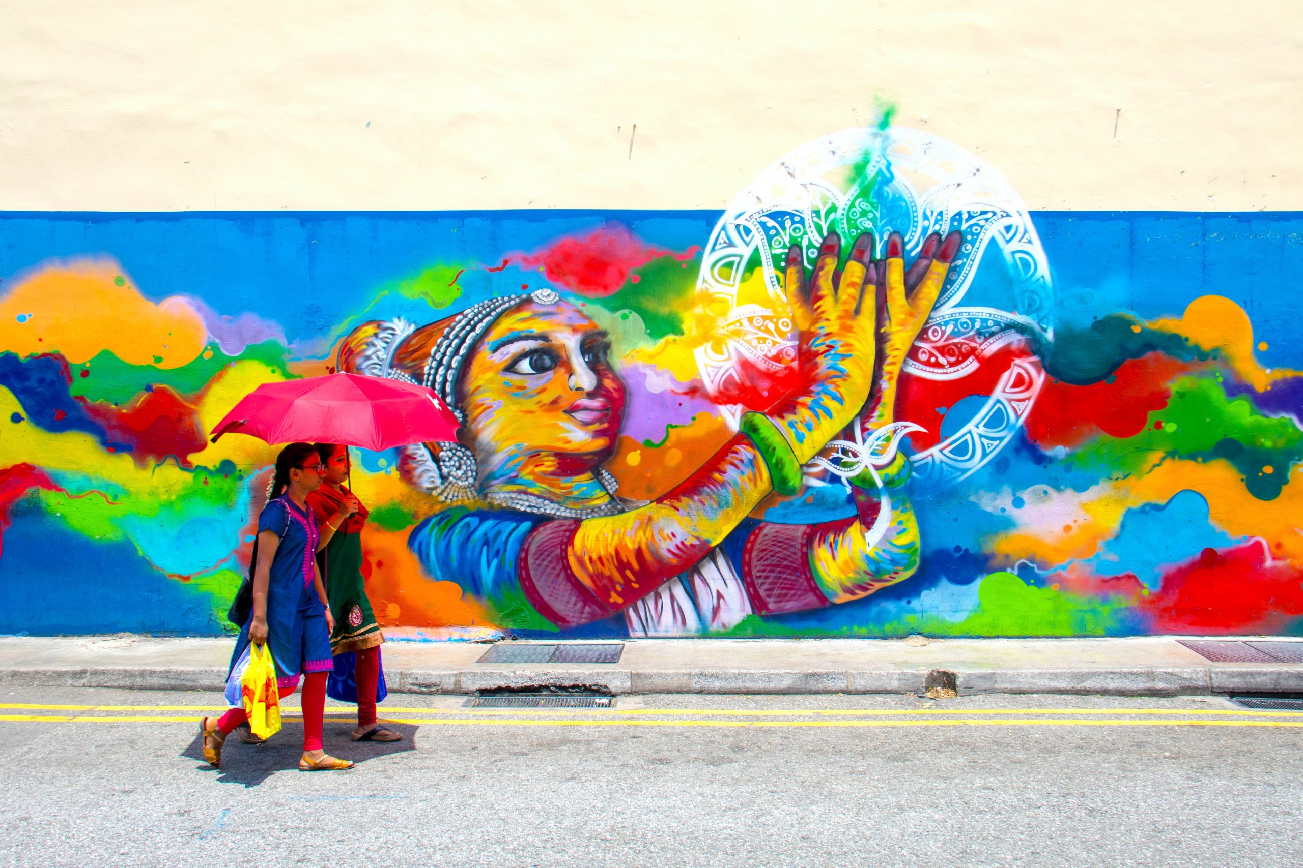 two girl holding umbrella while walking beside graffiti